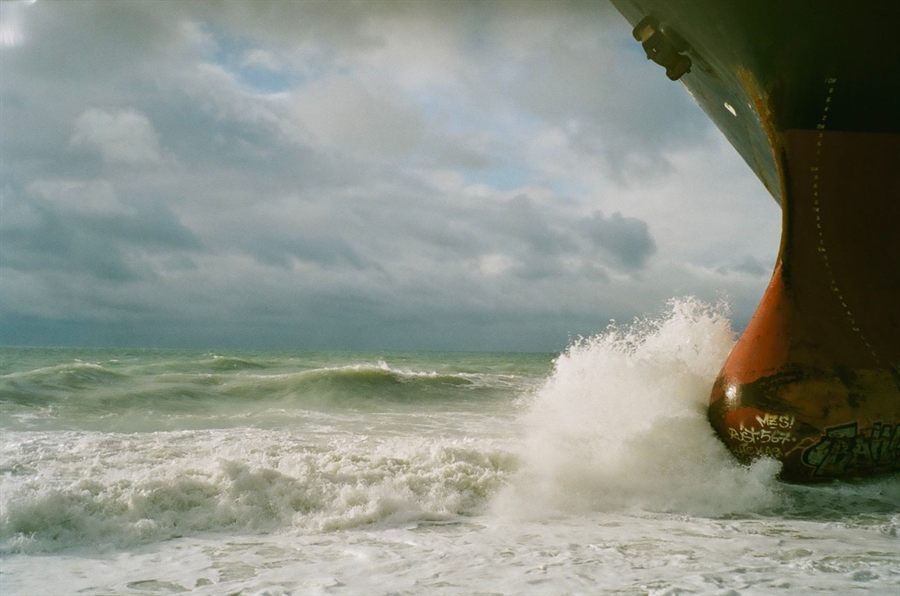 Ship bow breaking through ocean waves under a cloudy sky